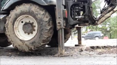 Yoldaki tamirat işleri. Traktör sürekli çalışan çıkıntıların üzerinde duruyor, tekerlek dönüyor. İşçiler yolu onarıyor..