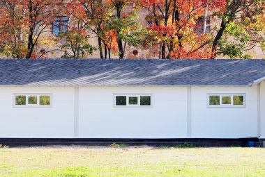 Beyaz duvar desenli ev, koyu pencereler, arka planda esnek gri fayanslar sonbahar ormanlarının çok renkli yaprakları.