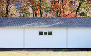 Beyaz duvar desenli ev, koyu pencereler, arka planda esnek gri fayanslar sonbahar ormanlarının çok renkli yaprakları.