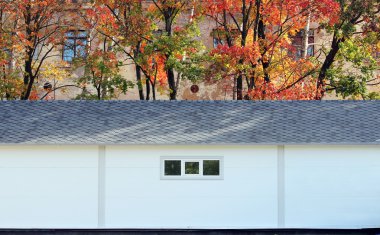 Beyaz duvar desenli ev, koyu pencereler, arka planda esnek gri fayanslar sonbahar ormanlarının çok renkli yaprakları.