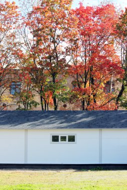 Beyaz duvar desenli ev, koyu pencereler, arka planda esnek gri fayanslar sonbahar ormanlarının çok renkli yaprakları.