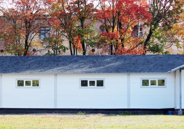 Beyaz duvar desenli ev, koyu pencereler, arka planda esnek gri fayanslar sonbahar ormanlarının çok renkli yaprakları.