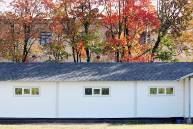 Beyaz duvar desenli ev, koyu pencereler, arka planda esnek gri fayanslar sonbahar ormanlarının çok renkli yaprakları.