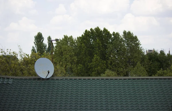 Grünes Dach des Hauses und alte Satellitenschüssel vor dem Hintergrund von Wald und Himmel — Stockfoto