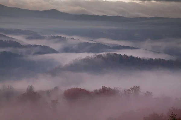 Rood-hued ochtend mist over rokerige bergen — Stockfoto