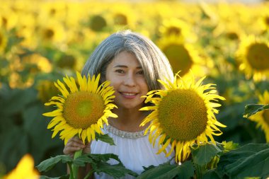 Yazın açan ayçiçeği tarlasında duran beyaz elbiseli kadın. Dixon, Solano County, Kaliforniya.
