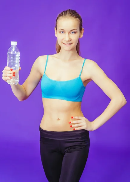 Giovane ragazza che tiene una bottiglia d'acqua su uno sfondo blu. Fitness, allenamento, esercizio fisico — Foto Stock