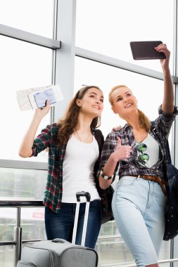 Havaalanında bavul ve tablet vasıl seyir ile iki kız stand. Arkadaş grubu bir gezi