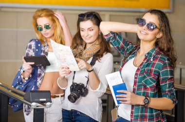 Üç genç kadın istasyonu veya havaalanında tutan bir kamera, kart, bir pasaport, bir tablet. Avrupalılar. 