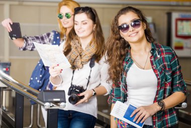 Üç genç kadın istasyonu veya havaalanında tutan bir kamera, kart, bir pasaport, bir tablet. Avrupalılar. 