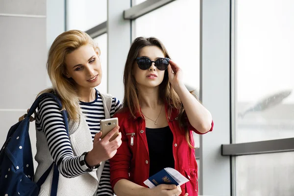 Terminal bir bavul, bir sırt çantası ve bir pasaport ile ayakta iki güzel kadın telefona bakmak