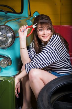 retro car araçları ile yakınındaki garajda bir beyzbol şapkası genç çekici kadın oturuyor. Kız holding pense