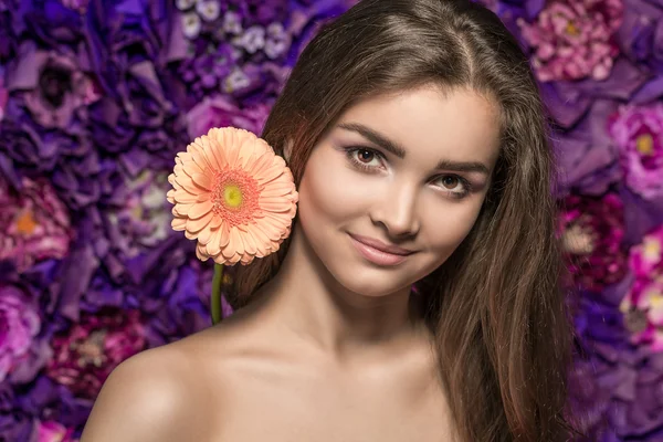 Retrato de bela jovem sorridente com uma flor gerbera.on a flor parede de fundo — Fotografia de Stock