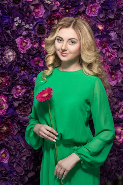 Retrato de uma bela mulher loira que está olhando para a câmera e sorrindo na flor da parede de fundo — Fotografia de Stock