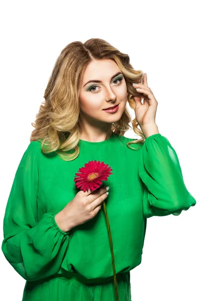 Bela mulher loira em um vestido verde dobrou as mãos perto do rosto e corrige penteado segurando flor de gerbera — Fotografia de Stock