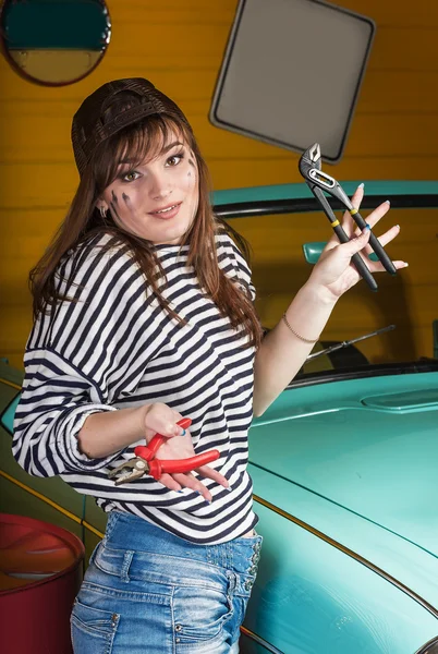 Attraente donna bruna in una giacca a righe nel garage vicino alla macchina retrò, nelle mani che tengono gli strumenti . — Foto Stock