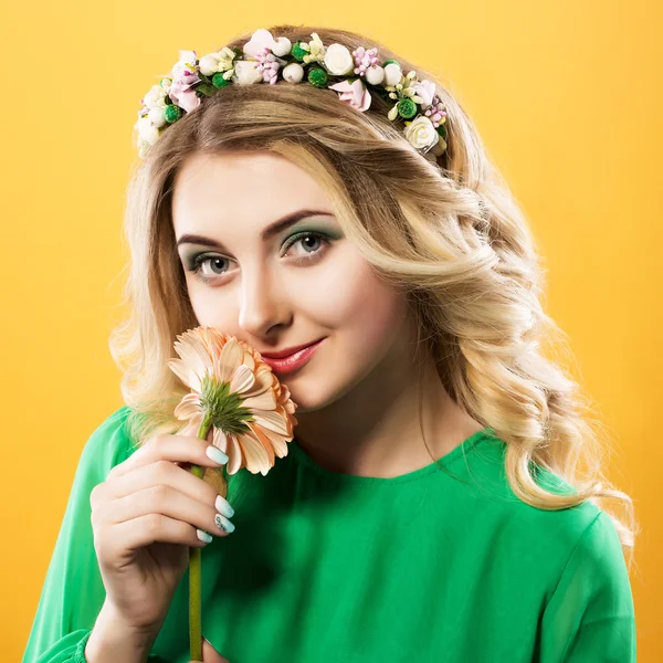 Bela mulher loira com uma grinalda em vestido verde, mantendo a flor perto de lábios em um fundo amarelo . — Fotografia de Stock