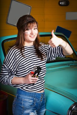 bir kap ve bir çizgili süveter gösteren esmer kadın başparmak yukarı ve tutan araçları retro car yakınındaki garajda