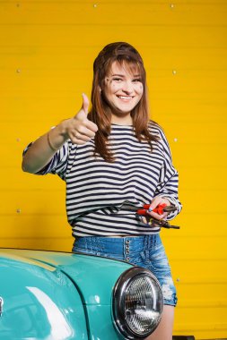 bir kap ve bir çizgili süveter gösteren esmer kadın başparmak yukarı ve tutan araçları retro car yakınındaki garajda