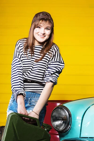 stock image woman in a cap and a striped sweater holding empty or full canister of gasoline in the garage near the retro car