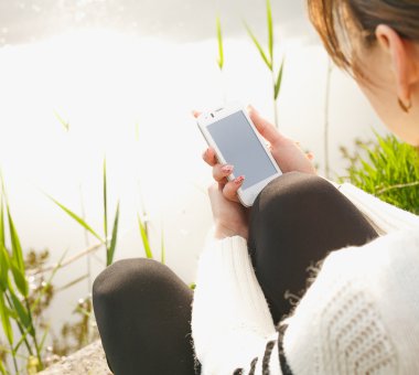 İstimal hareket eden telefon, çim üzerinde oturan güzel ve genç birbayan. Yaz fotoğraf. Kıyı görünümü.