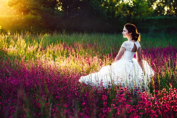Krásná nevěsta v květu pole. Dívka v bílých šatech s kyticí v letní pole při západu slunce — Stock fotografie
