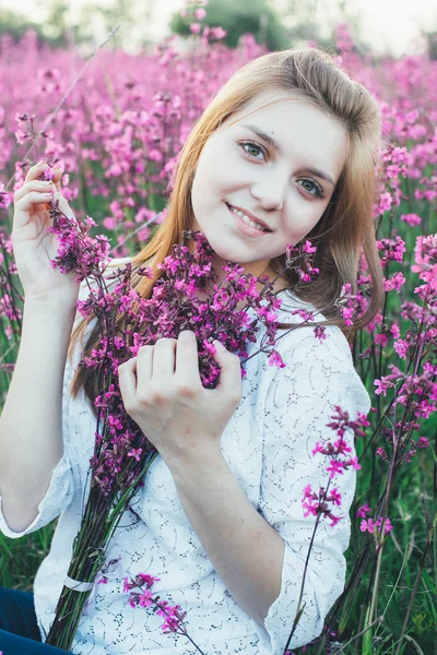 Schöne Braut in einem Blumenfeld. das Mädchen in einem weißen Kleid mit einem Strauß in einem Sommerfeld bei Sonnenuntergang — Stockfoto