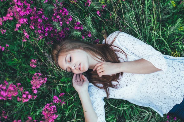 Όμορφο κορίτσι ξαπλωμένο στο γρασίδι και λουλούδια — Φωτογραφία Αρχείου