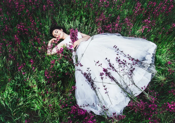 Vackra unga brud i fält, glad kvinna njuter flowers.beautiful tjej ligga i gräset och blommor — Stockfoto