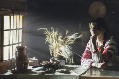 karanlık bir odada masada oturan geleneksel Ukrayna kostüm güzel ve genç birbayan. Işık ışınları