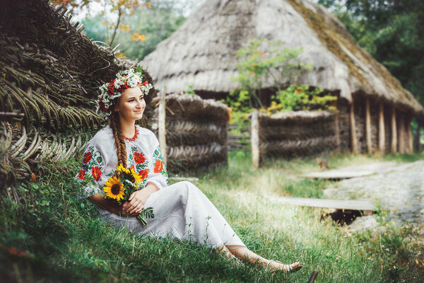 a young Ukrainian woman in traditional dress sits under a fence along the road