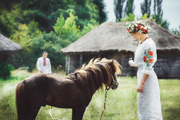 A young Ukrainian woman in traditional dress stands near a horse in a field — Stock Photo, Image