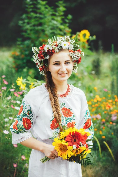 Una joven ucraniana en vestido tradicional con un ramo de pie sobre el fondo de flores silvestres —  Fotos de Stock