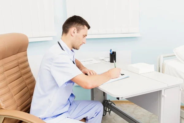 Retrato de um jovem médico em seu consultório médico. O local de trabalho do médico na clínica — Fotografia de Stock