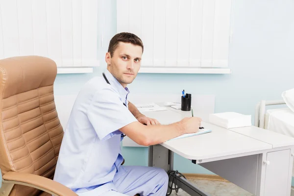 Retrato de um jovem médico em seu consultório médico. O local de trabalho do médico na clínica — Fotografia de Stock