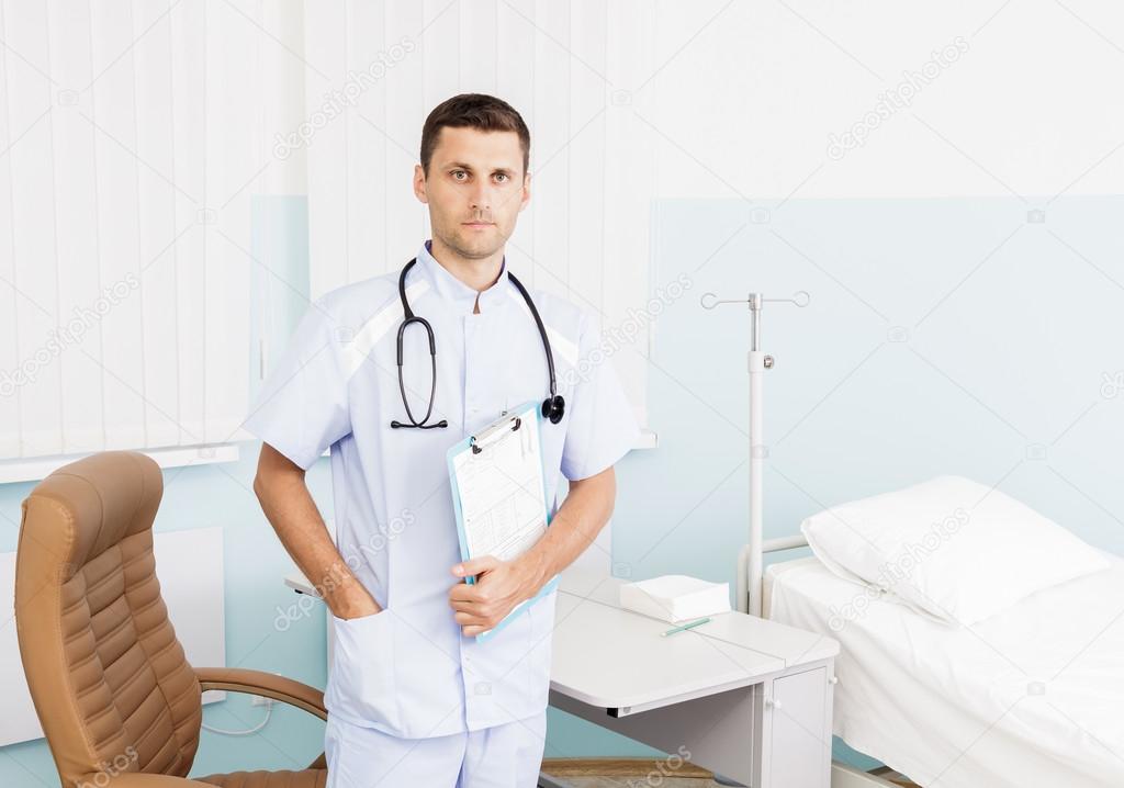 portrait of a young male doctor in his medical office. The workplace of the doctor at the clinic