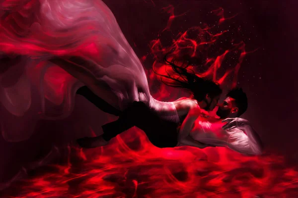 The couple is dancing or hugging in the pool underwater. A girl in a dress with a long train and a guy swim underwater. Red background. The kind of fire.