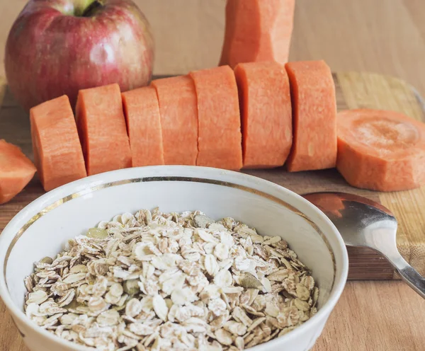 Haferflocken und Löffel, geschnittene Karotten, Apfel — Stockfoto