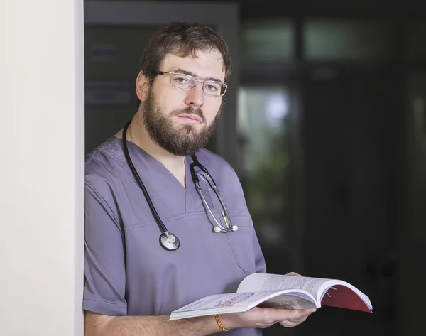 Barbudo médico masculino em óculos com um livro na mão no lobby — Fotografia de Stock