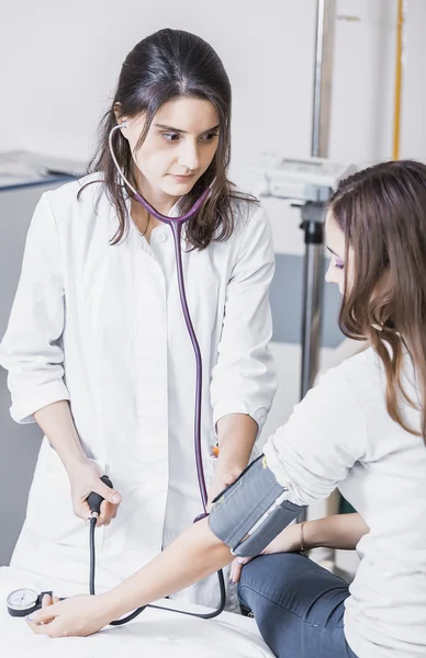 Beautiful girl doctor in a white coat checks the blood pressure in the girl on the bed — Stockfoto