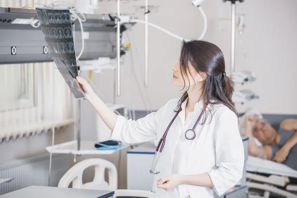 Mooi meisje arts in een witte vacht onderzoekt X-ray foto van de patiënt om het probleem te identificeren. Professionele gesprek, raadpleging van artsen. De werkzaamheden van de conferentie — Stockfoto