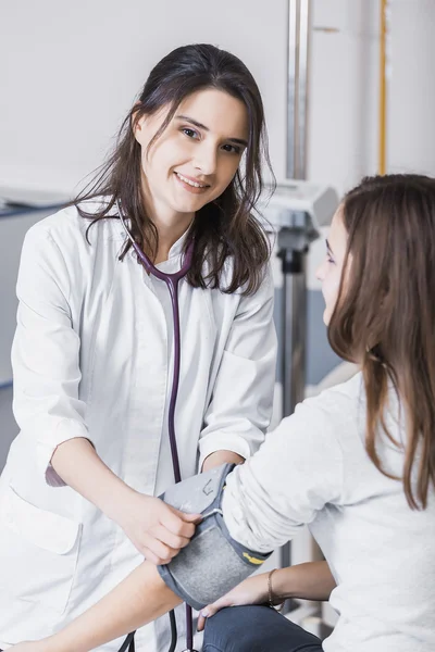 Красивая девушка врач в белом халате проверяет кровяное давление в девушке на кровати — стоковое фото