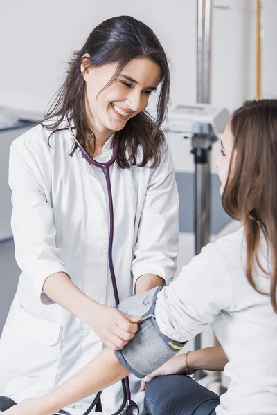 Beautiful girl doctor in a white coat checks the blood pressure in the girl on the bed — Stockfoto