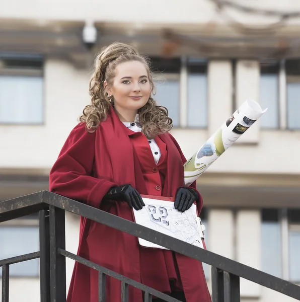 Jonge mooie vrouw architect in een rood jasje reputatie in de buurt van de reling met de tekeningen lestnitsy. Student — Stockfoto