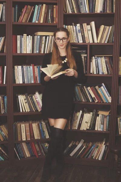 Όμορφη κοπέλα με ένα μαύρο φόρεμα στέκεται στη βιβλιοθήκη με βιβλία — Φωτογραφία Αρχείου