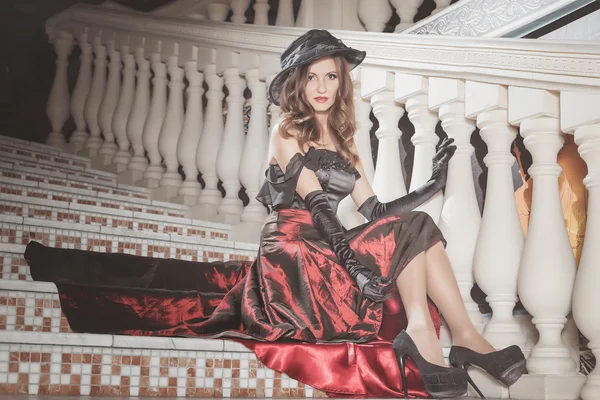 Красивая элегантная женщина в красно-черном платье сидит на винтажной лестнице в замке — стоковое фото