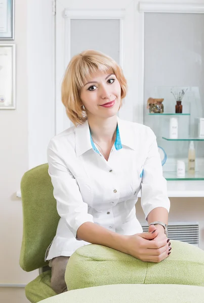 beautiful young beautician sitting in his office in a white robe and waits for the patient. Beautiful woman doctor.