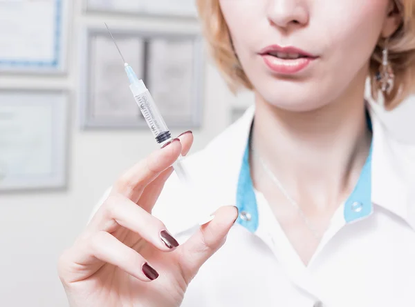 女性美容師は、オフィスで白いローブの永久的なそして唇付近に注射器の針を保ちます。注射器を持つ医師 — ストック写真