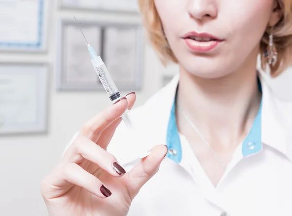  kadın güzellik uzmanı ofiste beyaz bir elbise içinde kalıcıdır ve dudaklar yakınındaki şırınga iğne tutar. Doktor şırınga ile