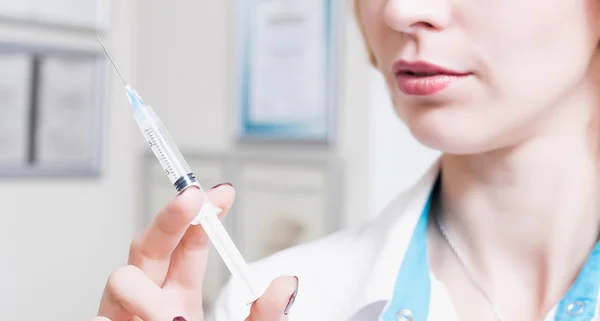  kadın güzellik uzmanı ofiste beyaz bir elbise içinde kalıcıdır ve dudaklar yakınındaki şırınga iğne tutar. Doktor şırınga ile